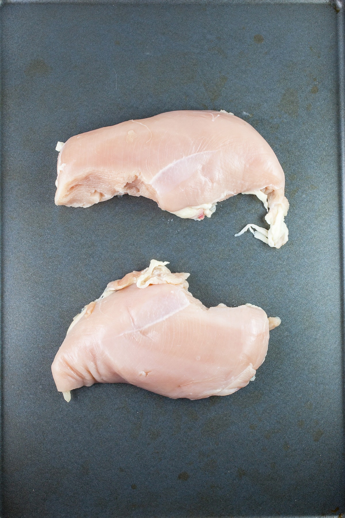 Raw chicken breasts on baking sheet.