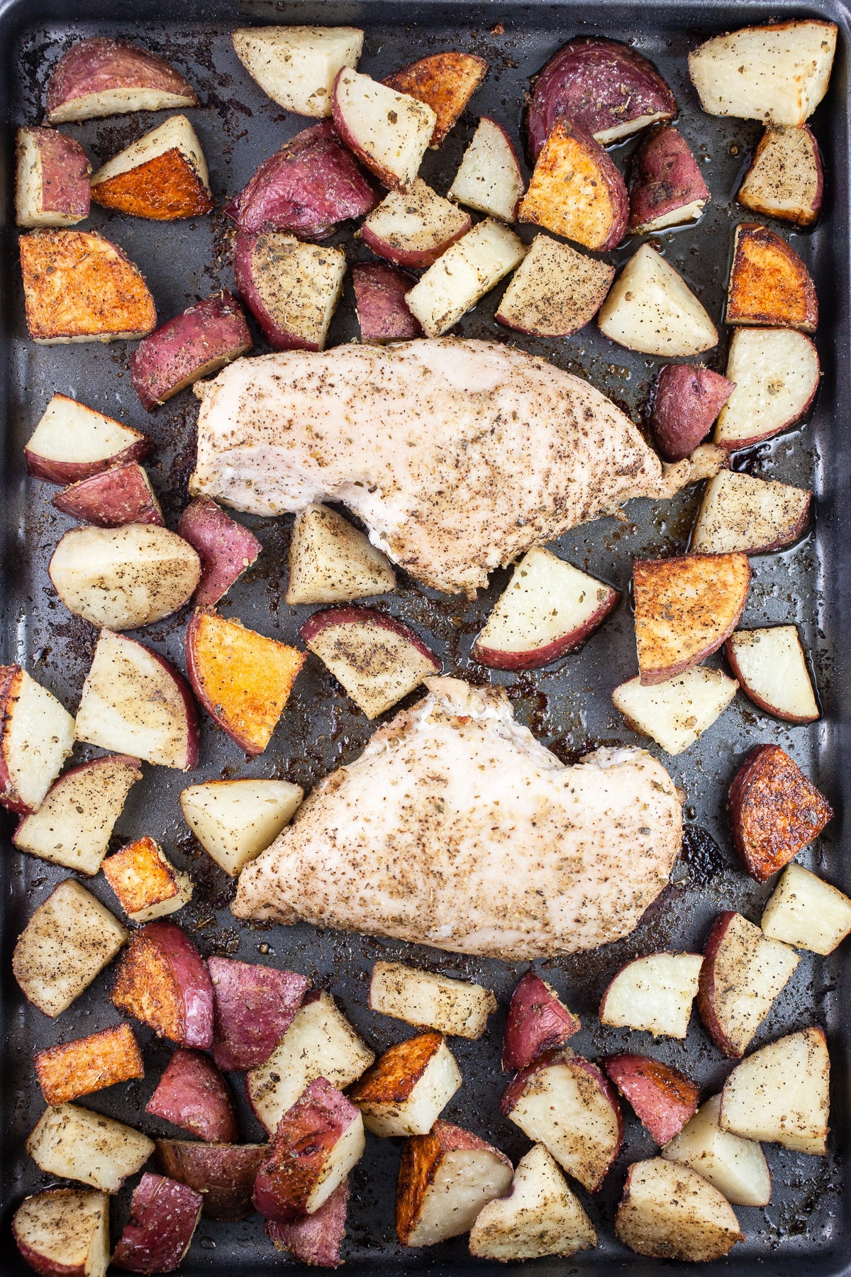 Cooked chicken breasts and diced red potatoes on baking sheet.