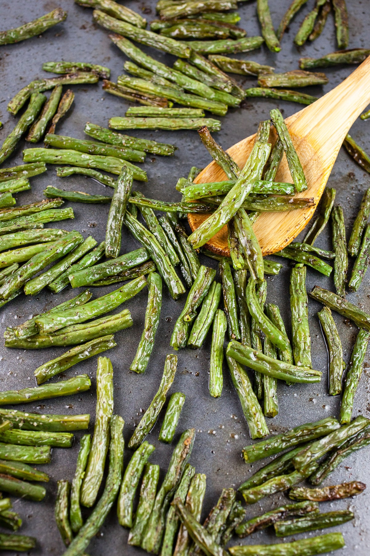 Roasted green beans on baking sheet with wooden spoon.