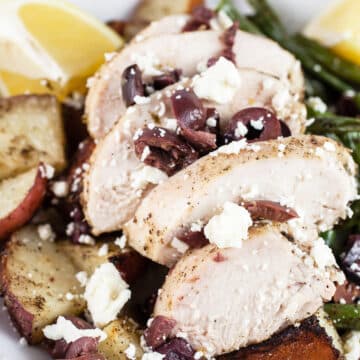 Sheet pan Greek chicken with potatoes, green beans, Kalamata olive, and feta in white bowl.