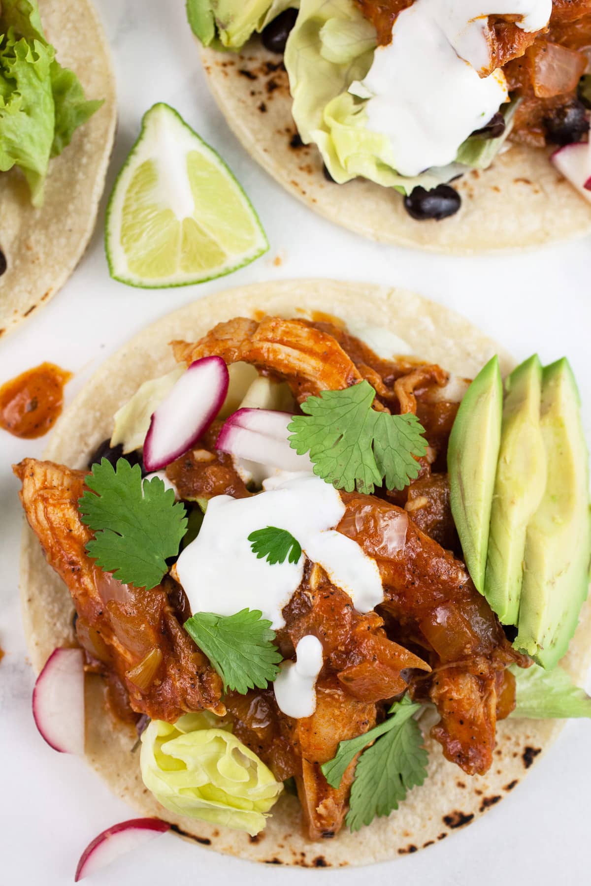 Chipotle chicken tacos on corn tortillas with lime crema, avocados, cilantro, and lime wedge.