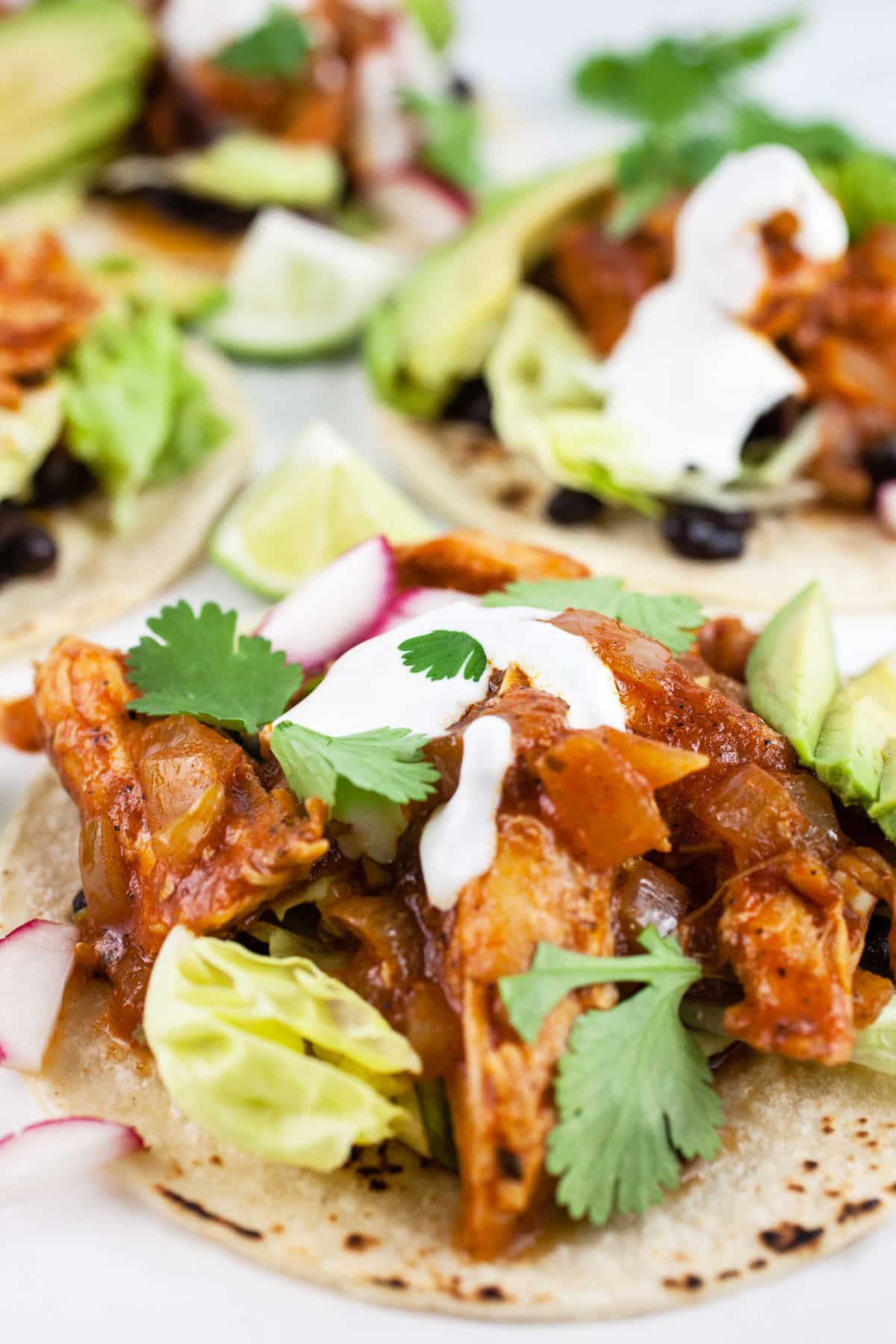 Shredded chicken tacos on corn tortillas with lime crema, avocadoes, greens, and cilantro.