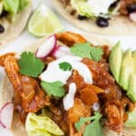 Shredded chipotle chicken tacos with lime crema, avocado, and cilantro on corn tortillas.