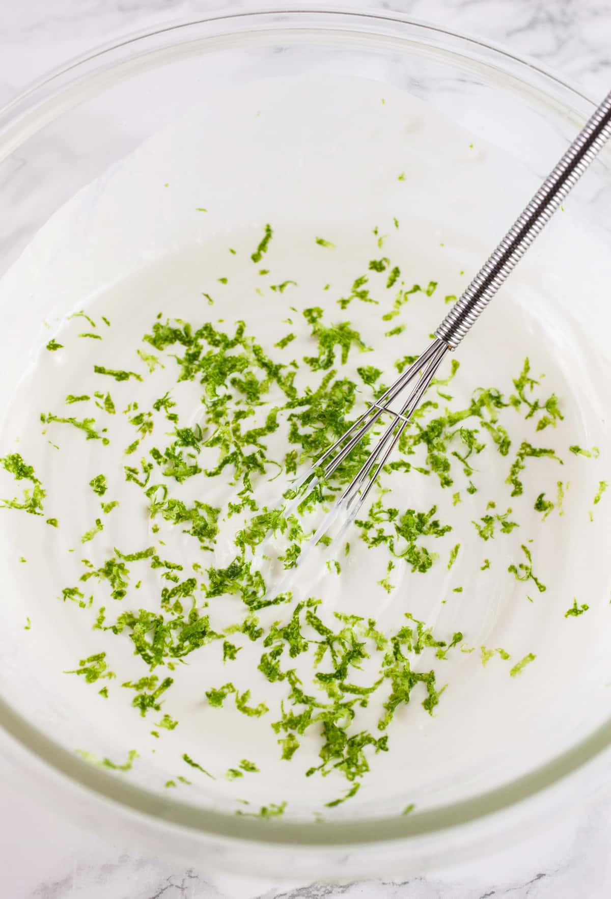Lime zest in glass bowl of Mexican crema with small whisk.