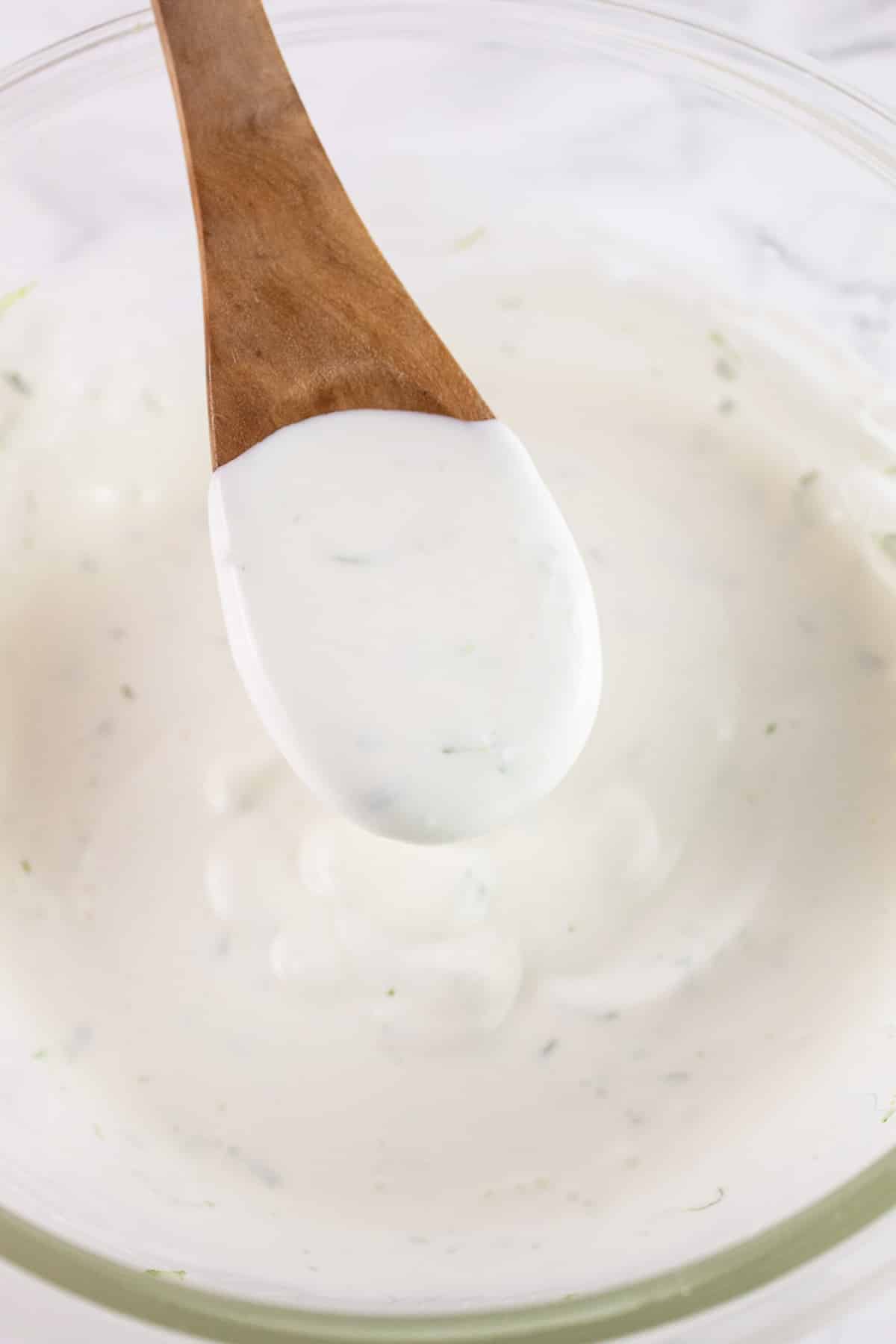 Wooden spoonful of lime crema lifted from glass bowl.