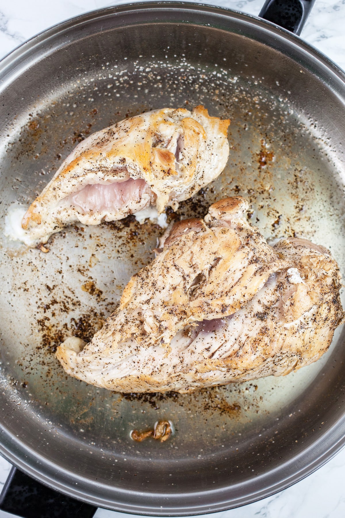 Chicken breasts sautéed with salt and pepper in skillet. 