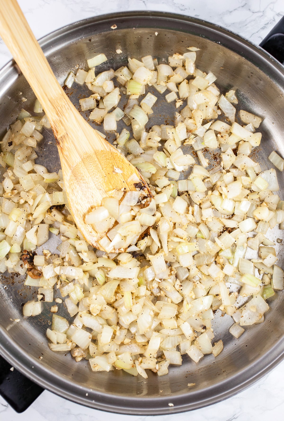 Minced garlic and onions sautéed in skillet with wooden spoon. 