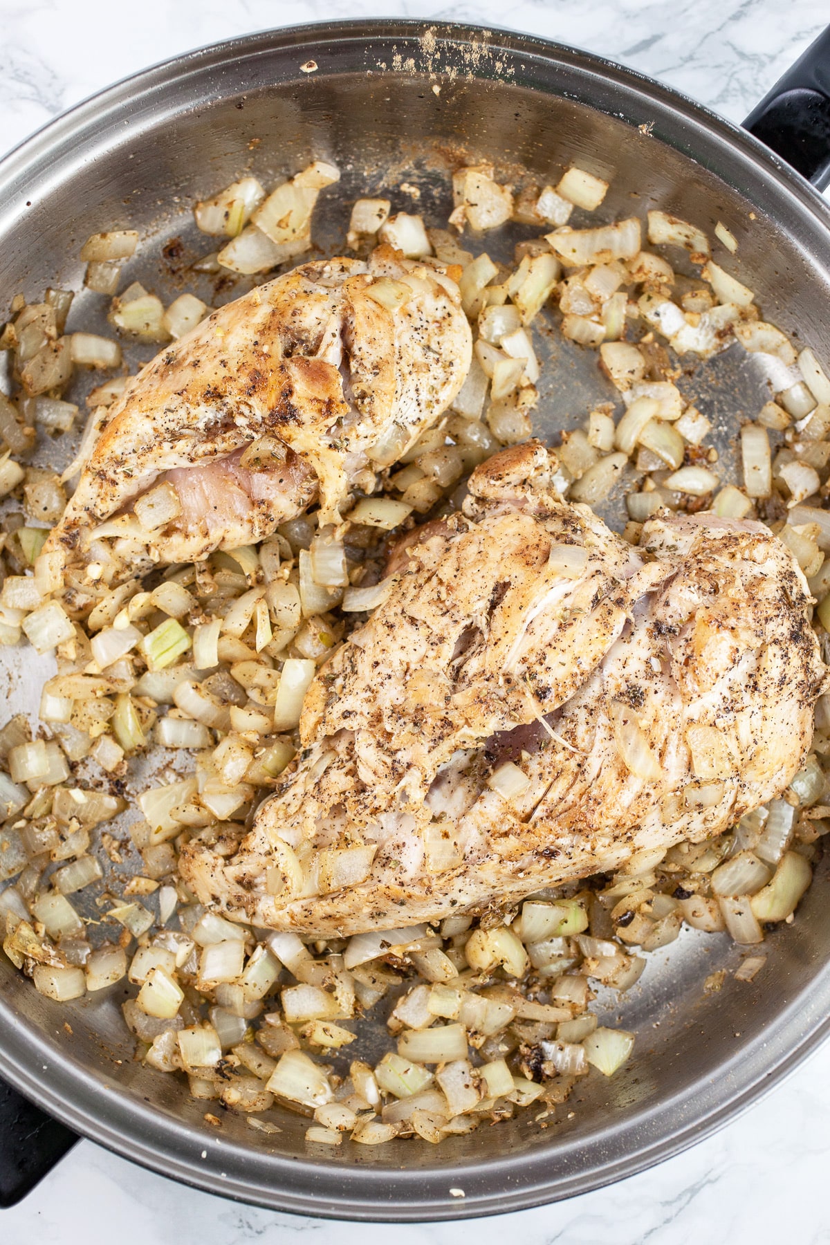 Chicken breasts sautéed with minced garlic ,onions, and spices in skillet.