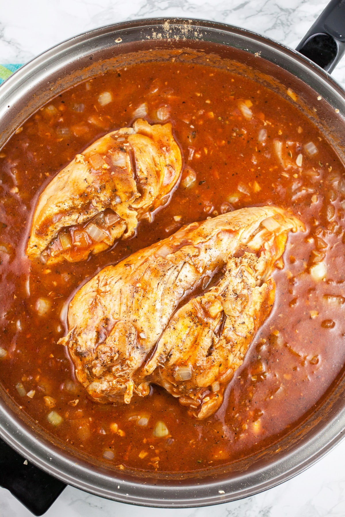 Chicken breasts simmered with red sauce in skillet.