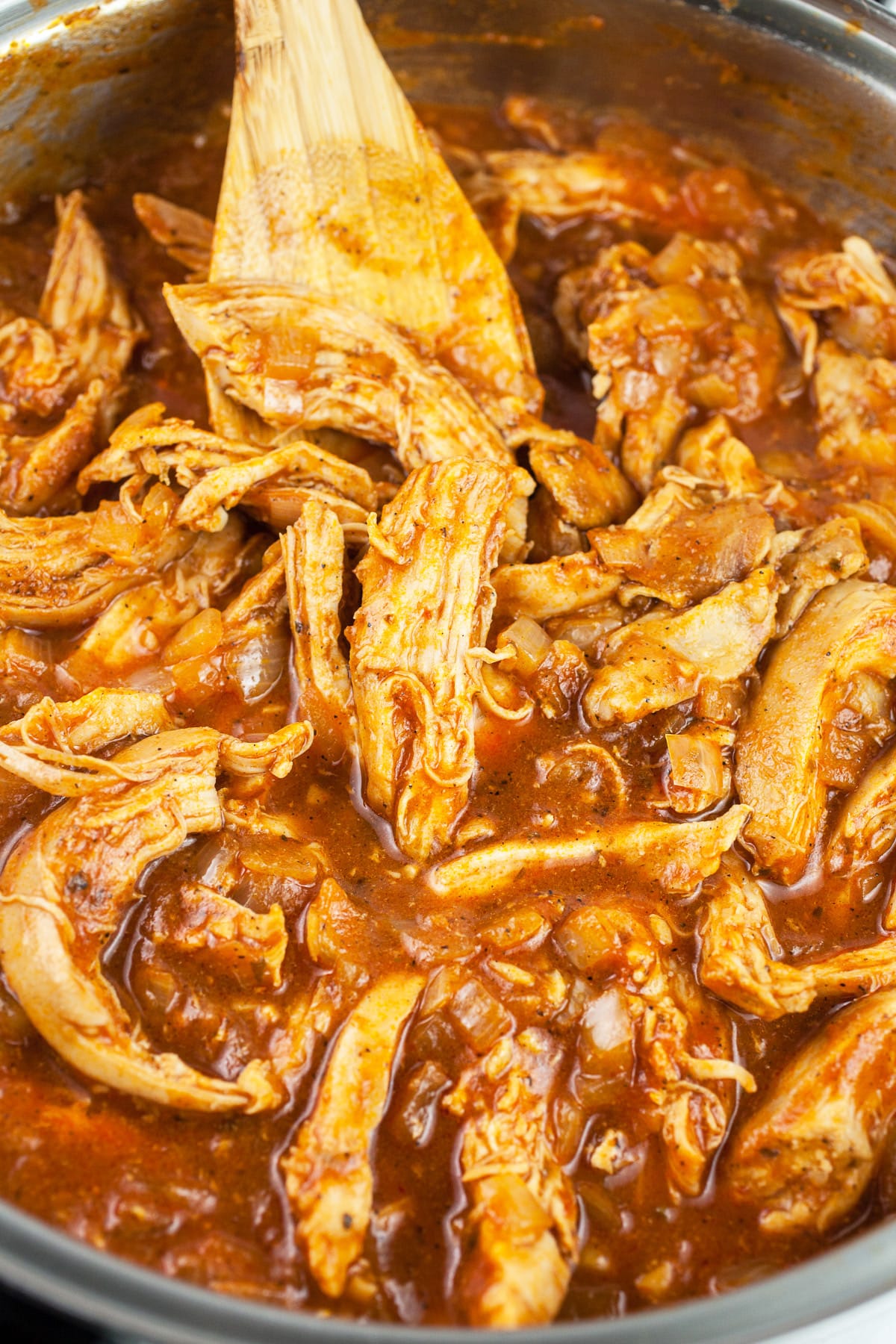 Shredded chipotle chicken in skillet with wooden spoon.