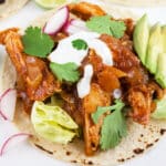 Shredded chipotle chicken tacos with lime crema, avocado, and cilantro on corn tortillas.