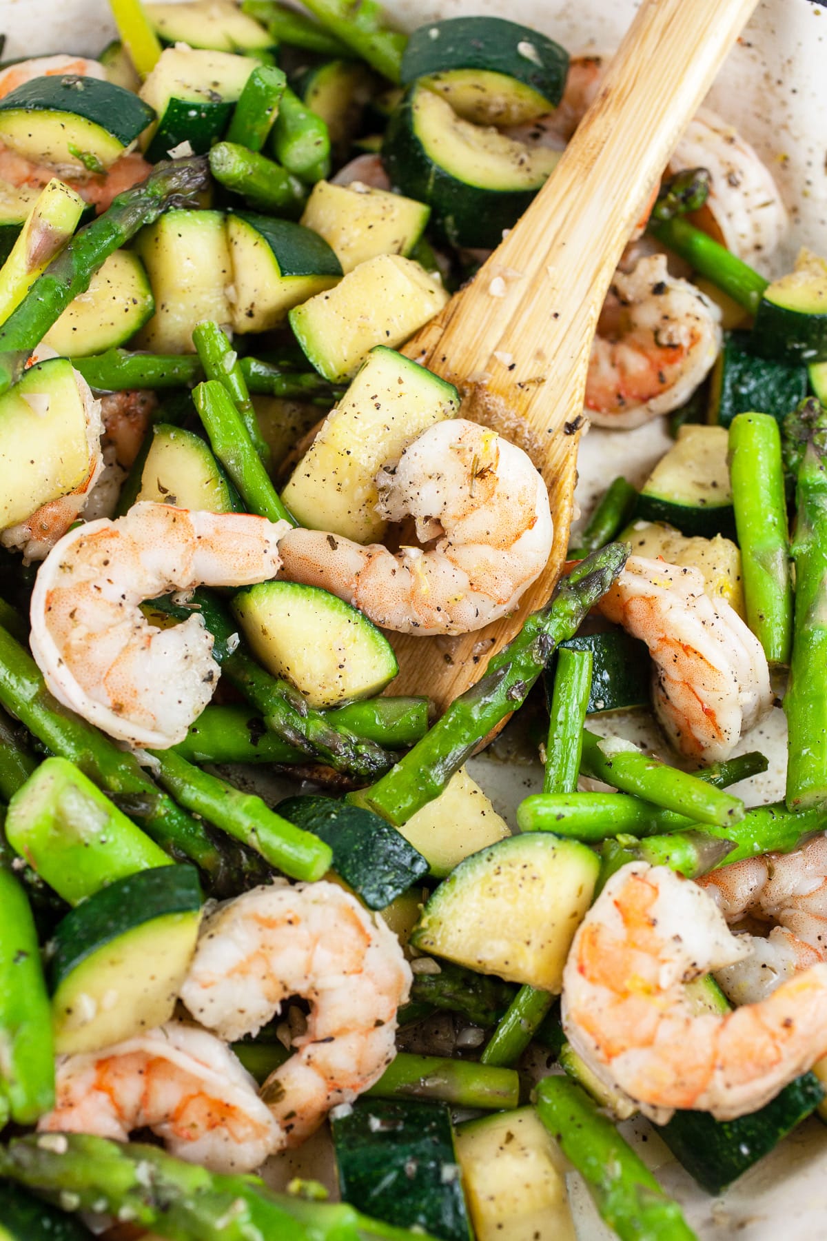 Sautéed shrimp, asparagus, and zucchini in skillet with wooden spoon. 