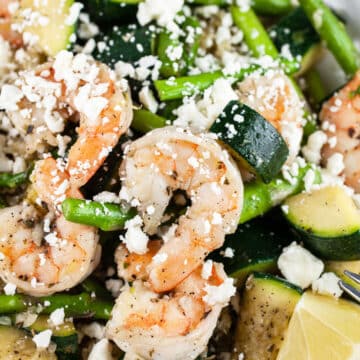 Skillet shrimp with asparagus, zucchini, feta cheese, and lemon wedges.