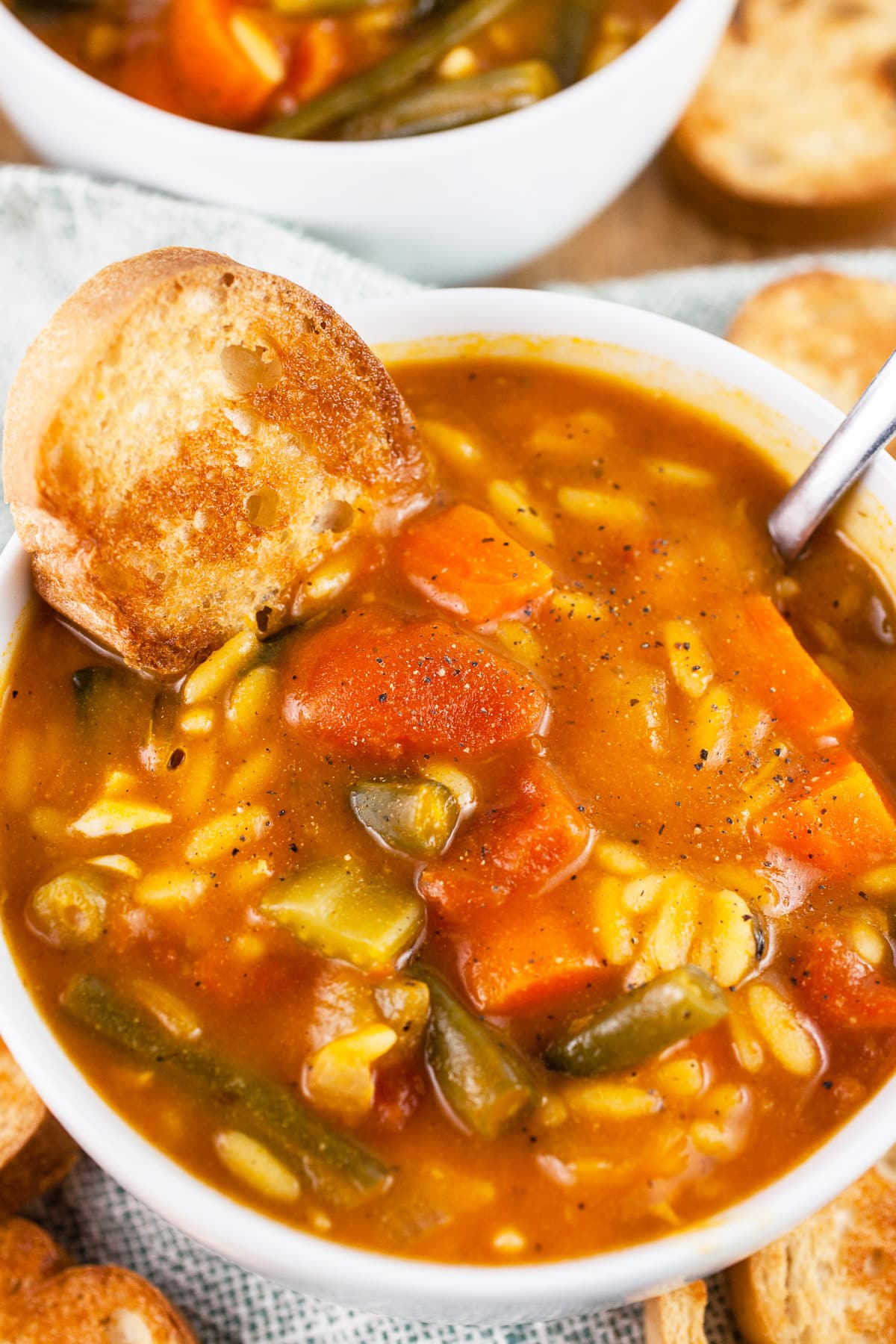 Vegetable orzo soup in bowl with toasted crostini bread.