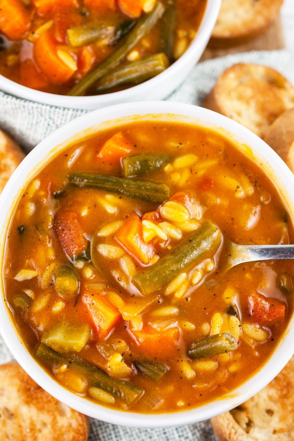 Vegetable orzo soup in white bowls with toasted crostini.