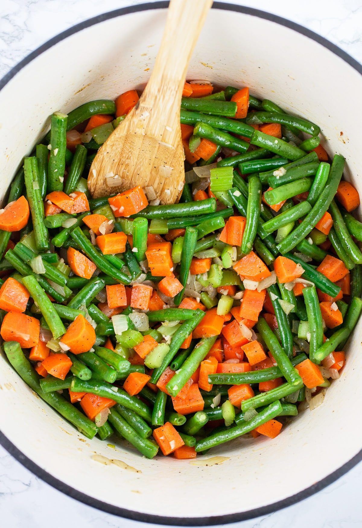 Green beans and carrots sautéed in Dutch oven with wooden spoon.