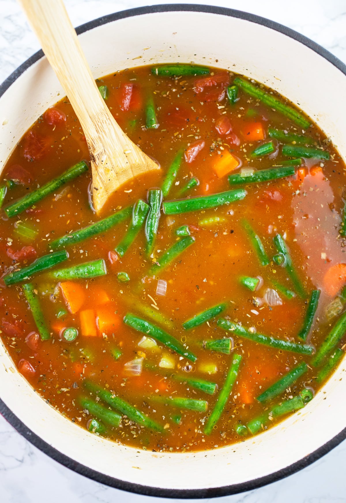 Vegetable broth added to veggies in Dutch oven with wooden spoon.