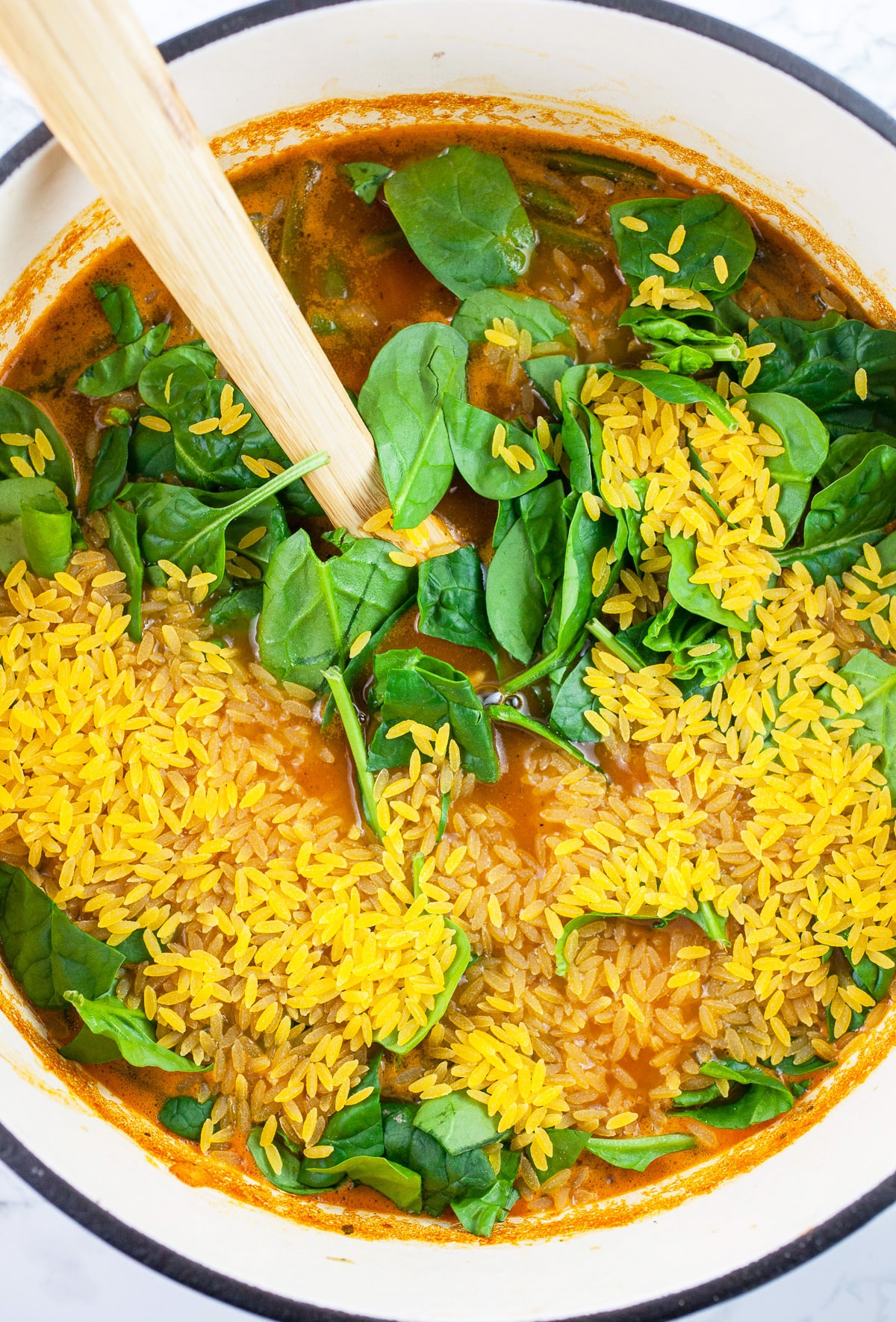 Uncooked orzo pasta and spinach added to soup in Dutch oven.