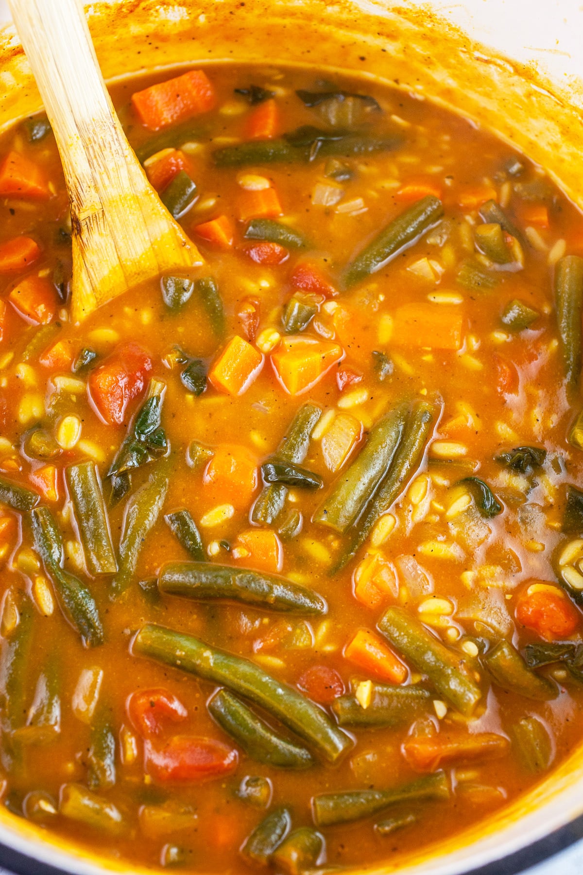 Vegetable orzo soup in Dutch oven with wooden spoon.