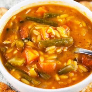 Vegetable orzo soup in white bowl with spoon.