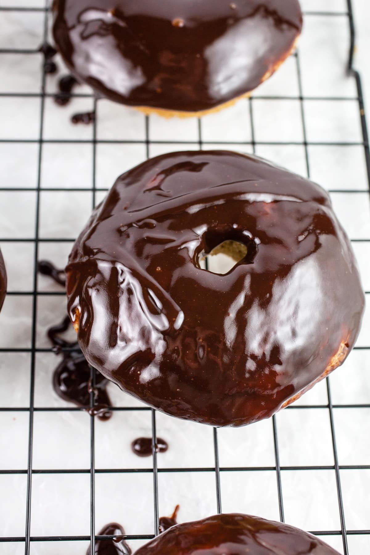 Doughnuts dipped in chocolate on cooling rack.