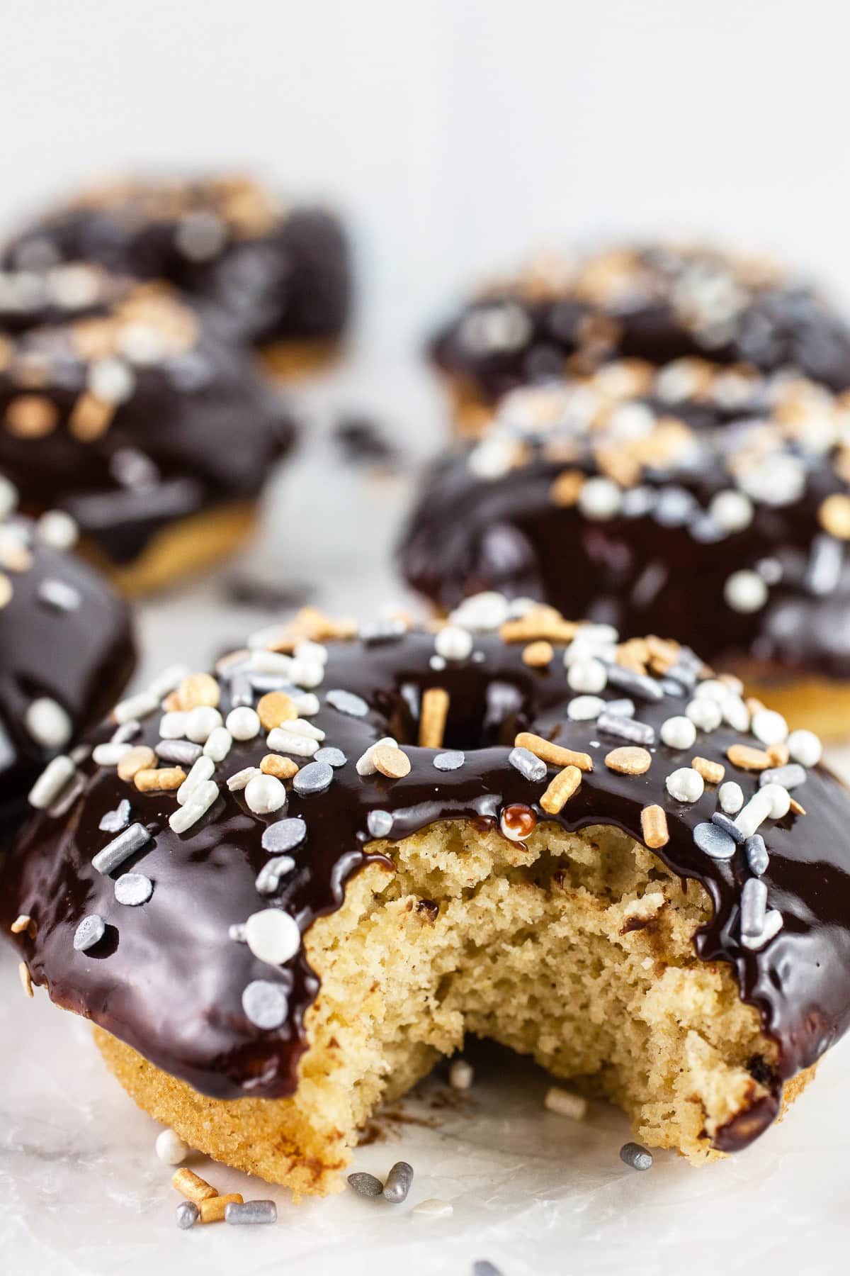 These Bailey's and Chocolate Glazed Doughnuts are the perfect St. Patrick's Day treat! They're easy to make and so fun to eat. These homemade doughnuts are baked and topped with a quick and simple Bailey's Irish Cream chocolate glaze. Doughnuts are one of my all-time favorite desserts and sweets! #doughnuts #baileys #chocolate #irishcream #stpatricksday Bite taken out of chocolate dipped Baileys sprinkled doughnuts.