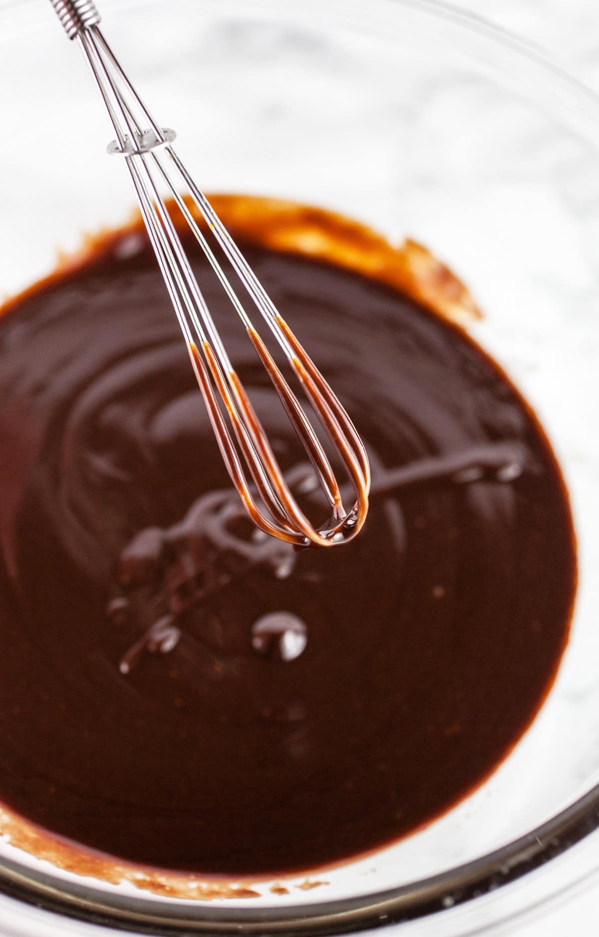 Metal whisk pulled out of glass bowl of chocolate ganache.