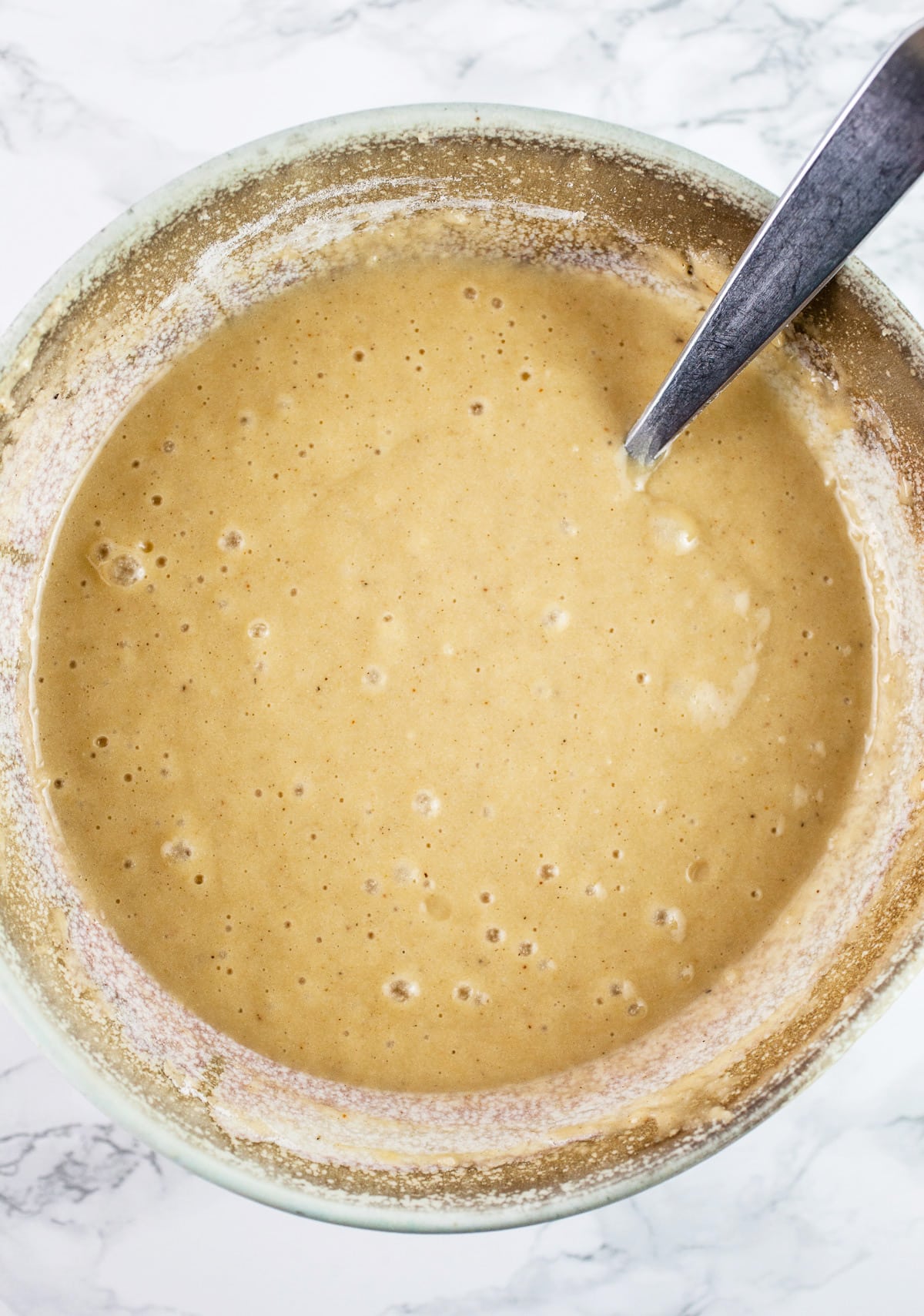 Wet ingredients with melted butter added in ceramic bowl with spoon.