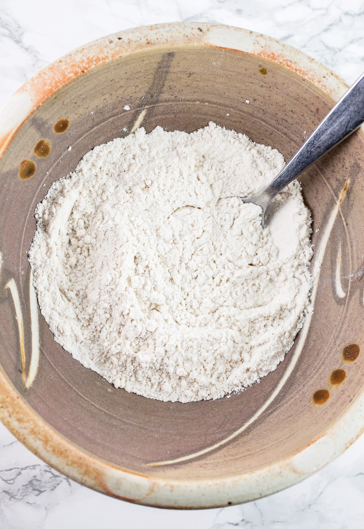 Dry ingredients in ceramic mixing bowl with fork.
