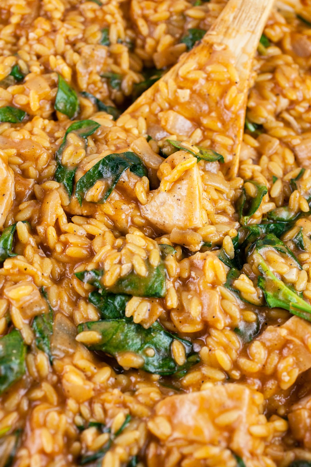 Cajun chicken spinach orzo pasta in skillet with wooden spoon.