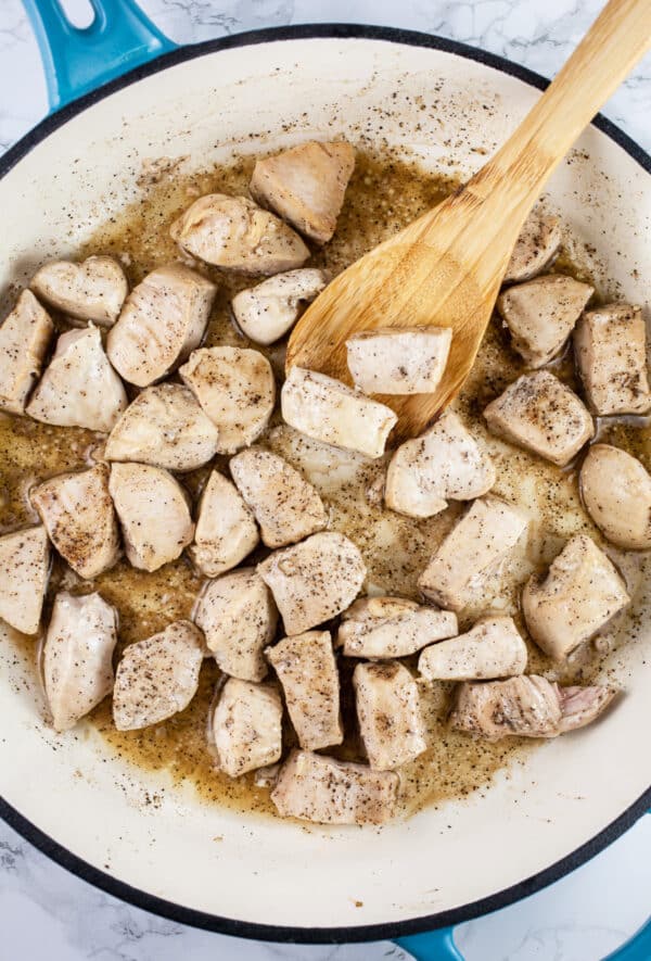 Diced chicken sautéed in skillet with wooden spoon.