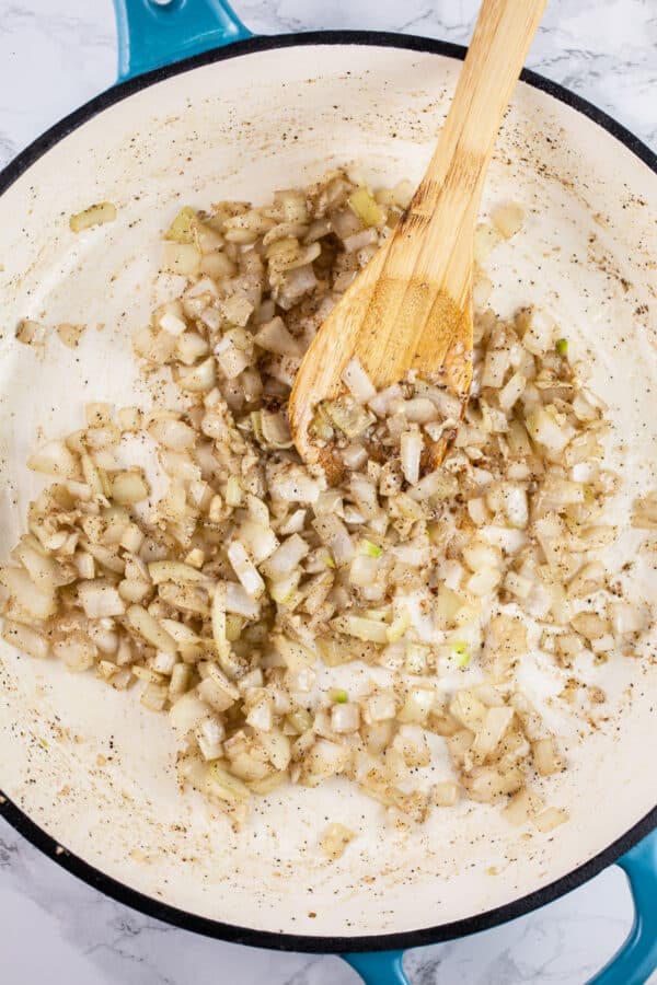 Minced garlic and onions sautéed in skillet with wooden spoon.