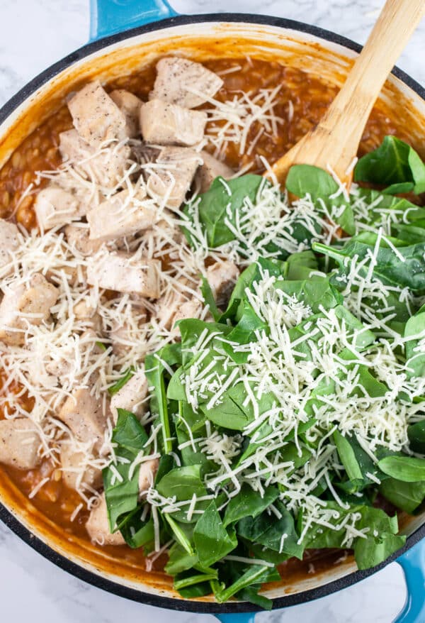 Cajun orzo pasta with cooked chicken, spinach, and Parmesan cheese with wooden spoon.