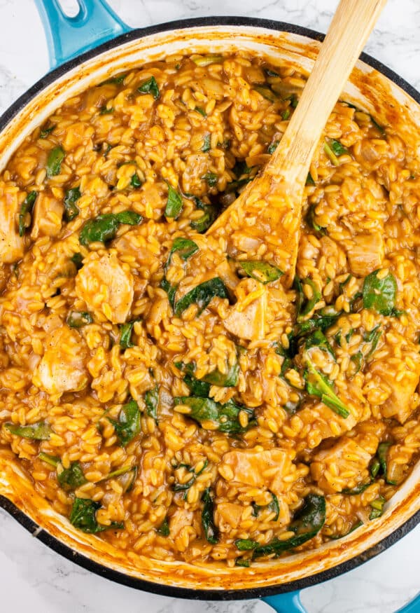 Cajun chicken orzo pasta in skillet with wooden spoon.