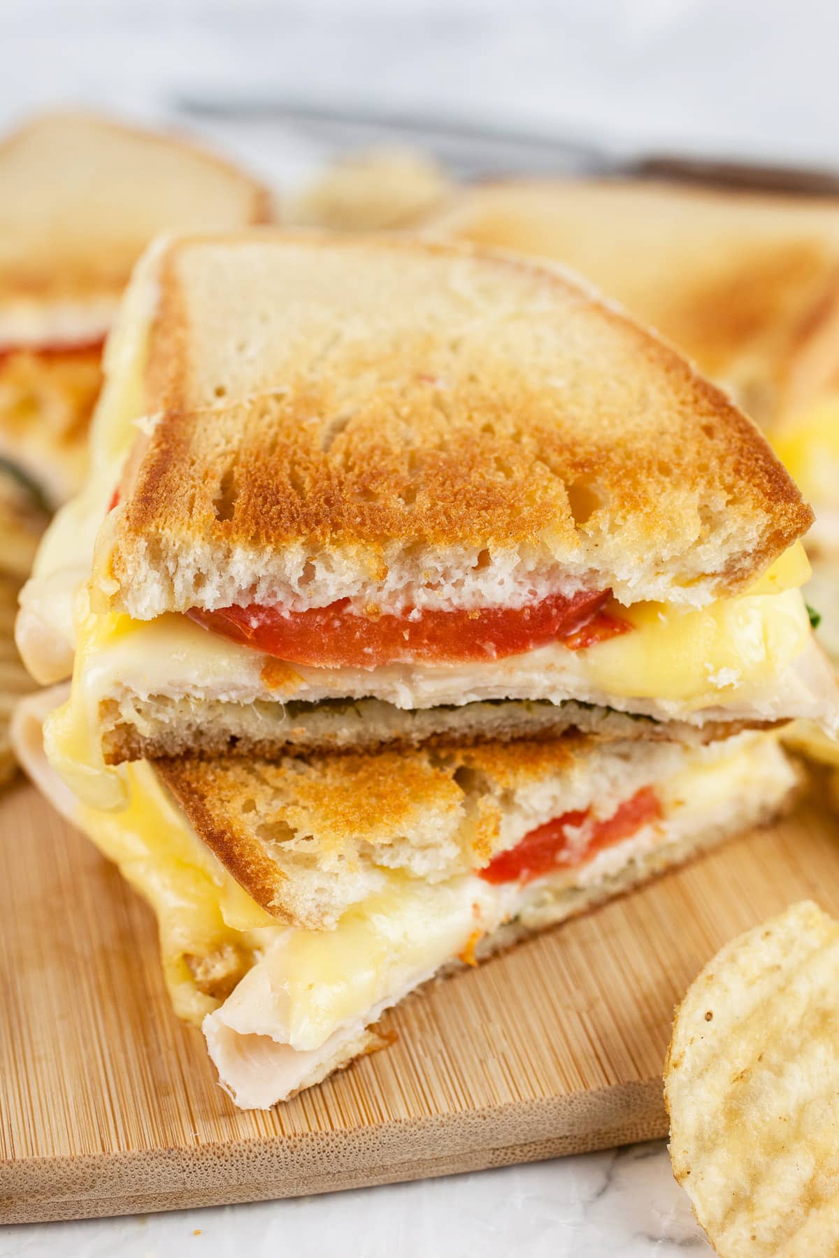 Gouda chicken grilled cheese sandwich cut in half on wooden board with knife.