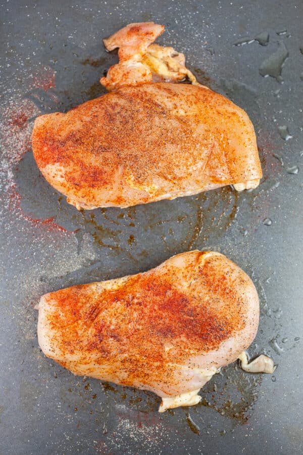 Uncooked spiced chicken breasts on baking sheet.