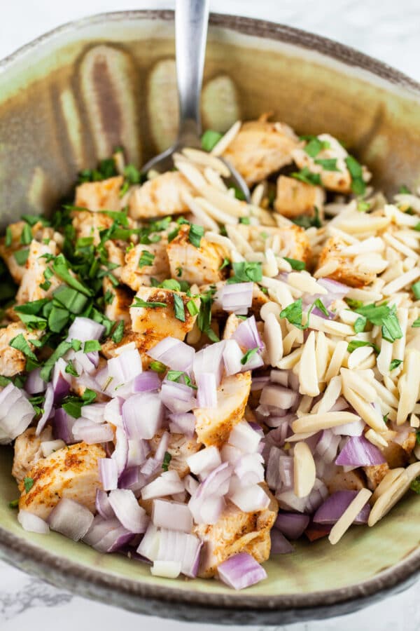 Diced chicken, slivered almonds, minced shallots, and tarragon in ceramic bowl with spoon.