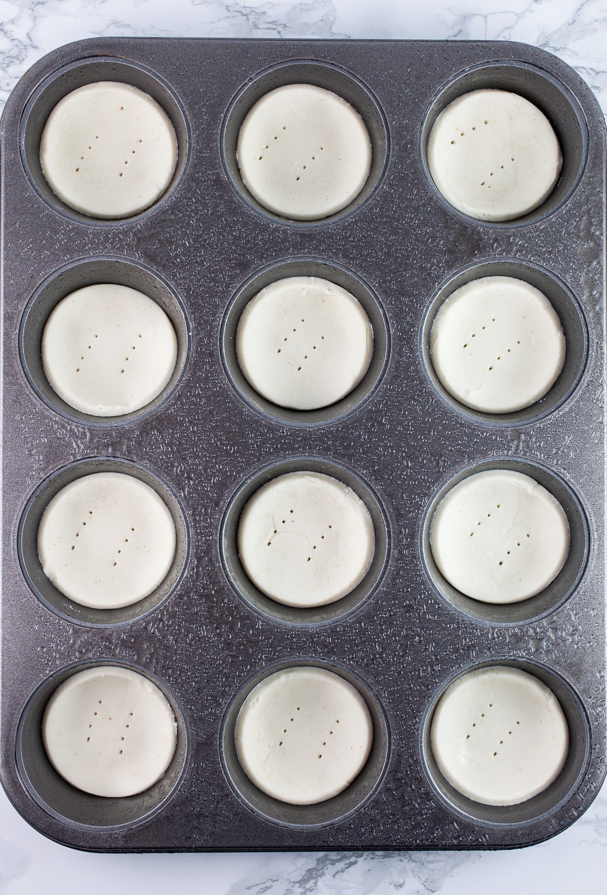 Uncooked Puff Pastry tartlets pierced with a fork in muffin tin.