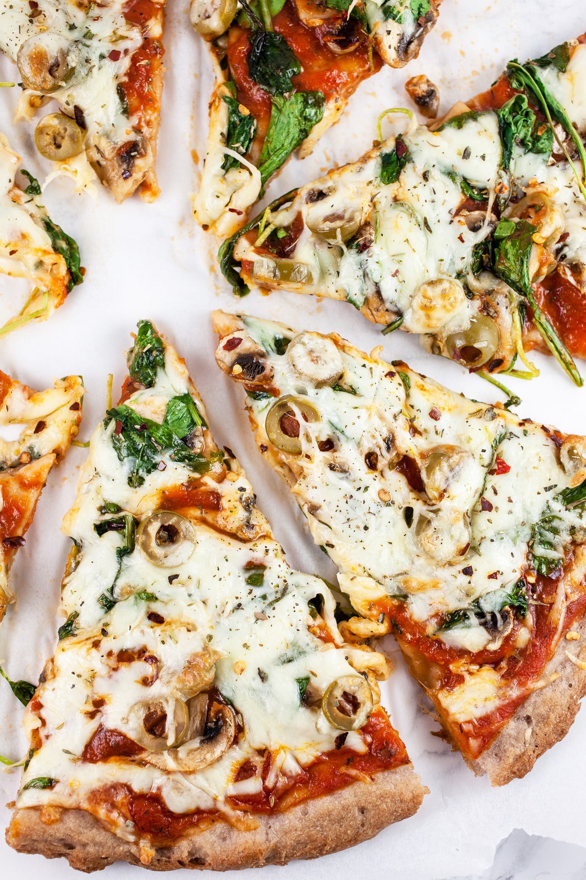 Sliced arugula mushroom pizza on white surface.