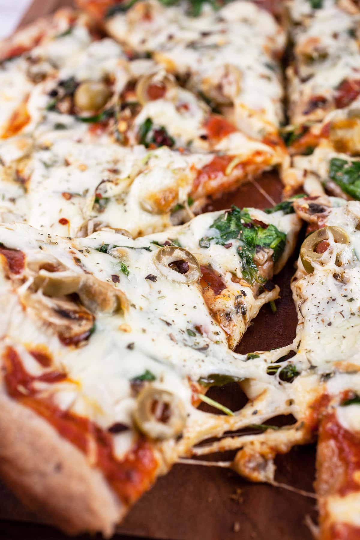 Slice of mushroom arugula pizza lifted from wooden cutting board.