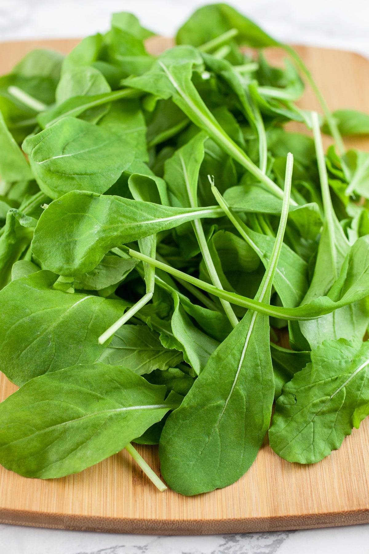 Arugula leaves on wooden cutting board.