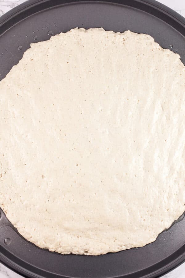 Uncooked gluten free pizza dough on round pizza pan.