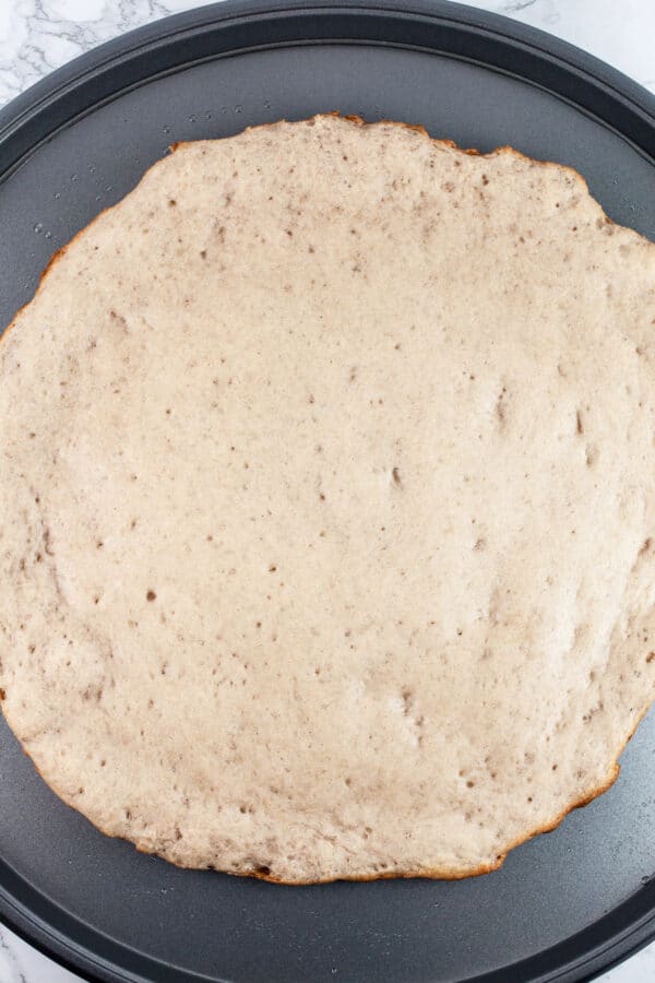 Parbaked gluten free pizza dough on round pizza pan.