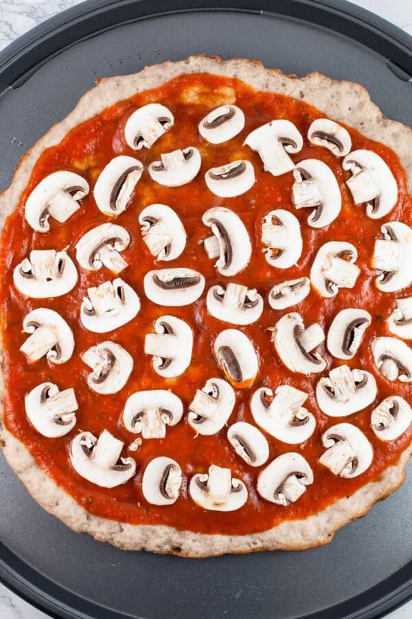 Sliced mushrooms and tomato sauce on pizza crust.