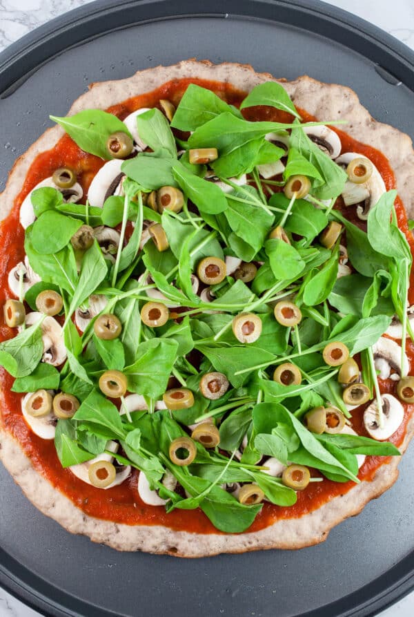 Tomato sauce, mushrooms, arugula, and green olives on pizza crust.