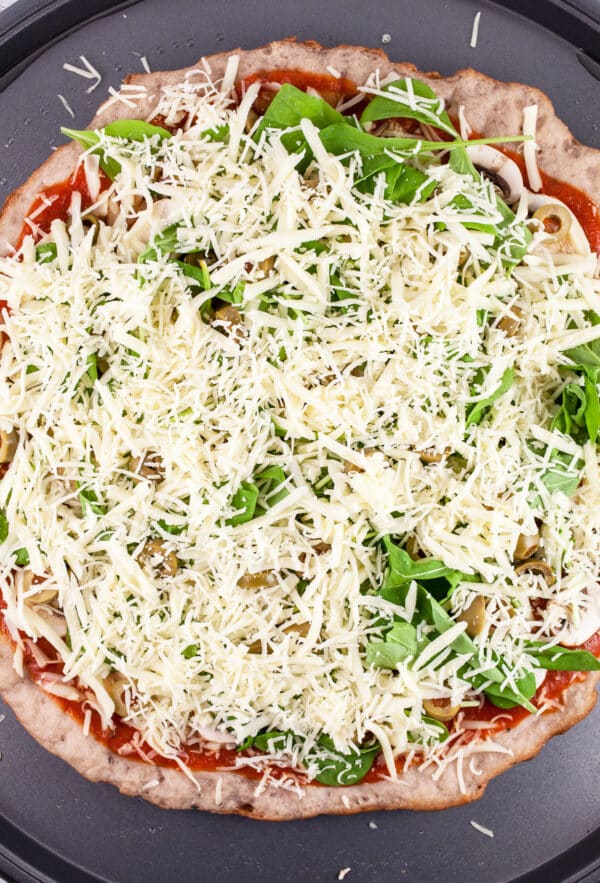 Unbaked pizza with shredded cheese on pizza crust.