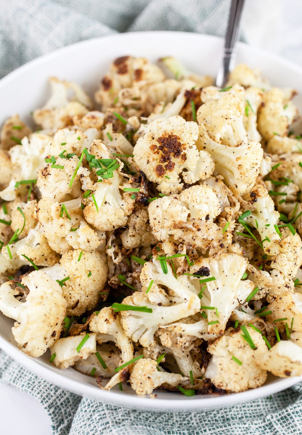 Garlic Parmesan roasted cauliflower with minced chives in white bowl with spoon.