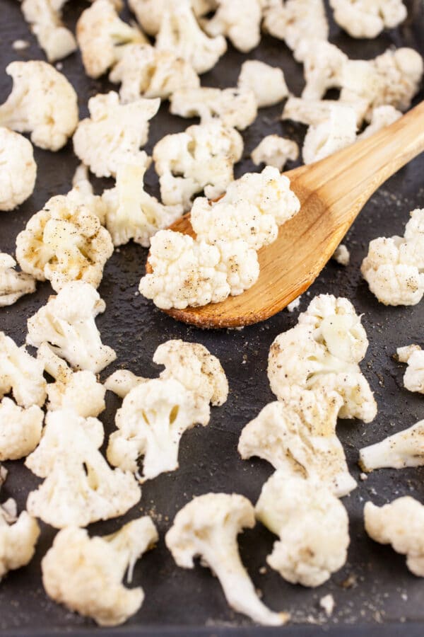 Uncooked cauliflower florets on baking sheet with wooden spoon.