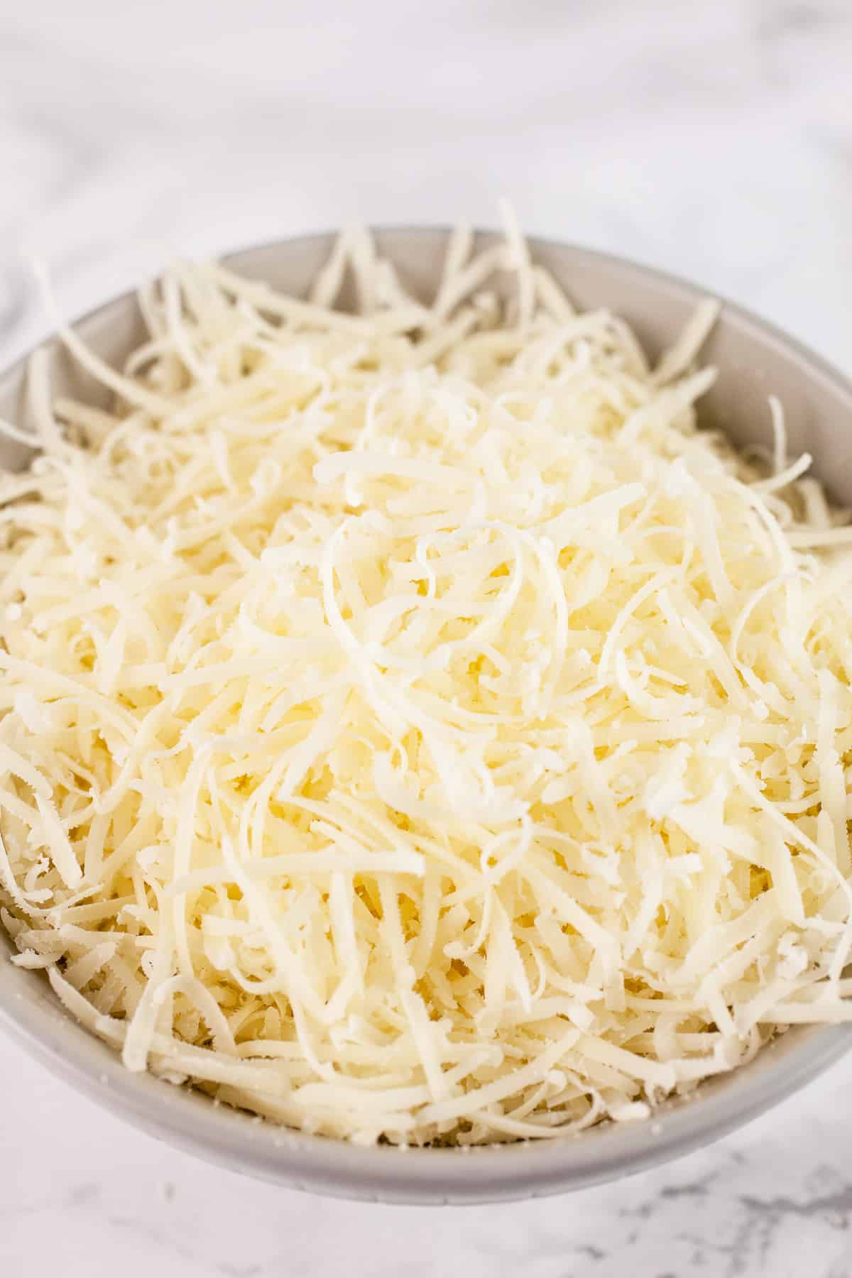 Shredded Parmesan cheese in small grey bowl on white surface.