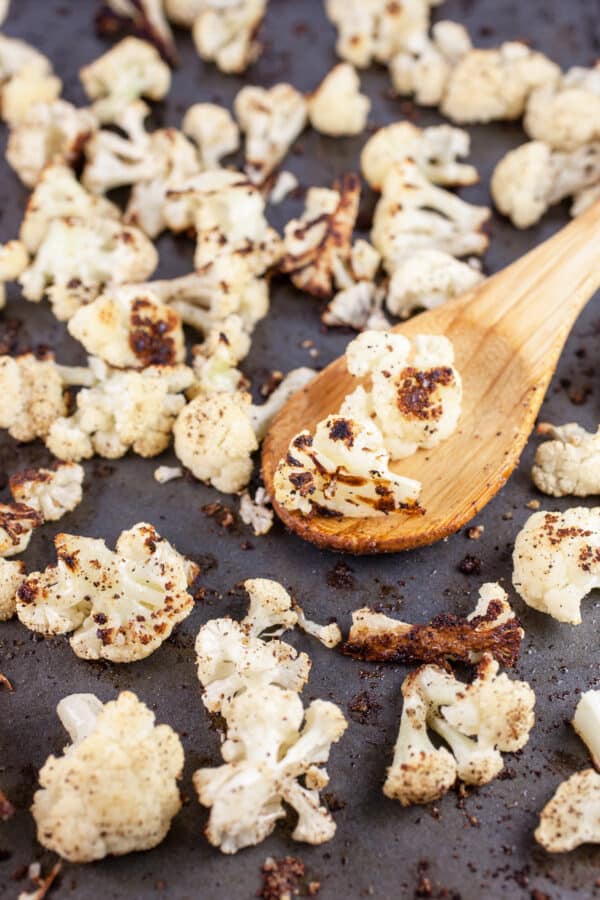 Roasted cauliflower florets on baking sheet with wooden spoon.